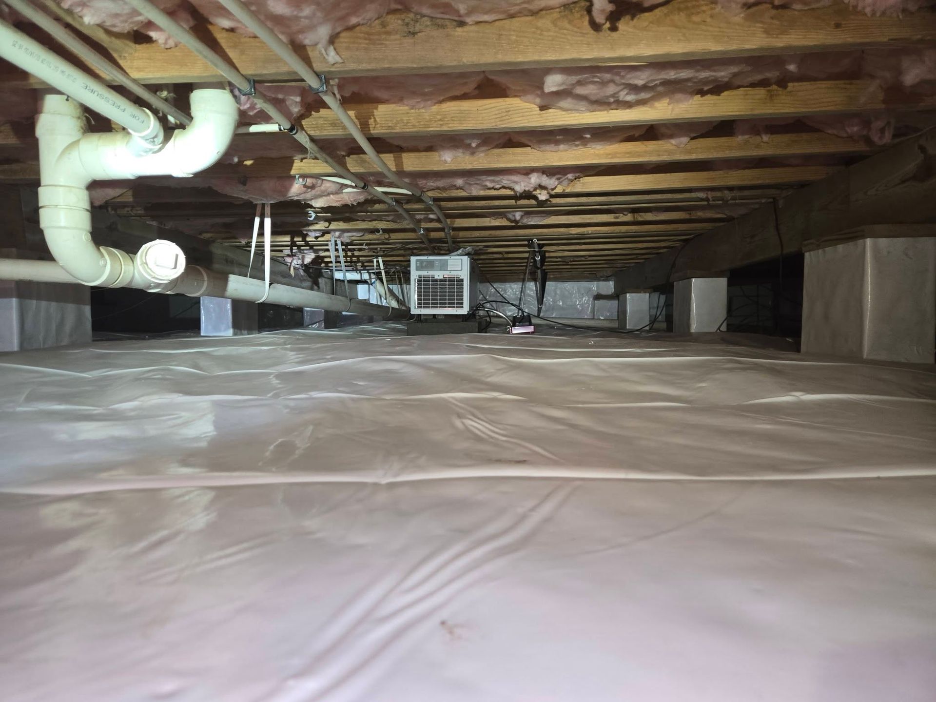 Plastic-covered crawl space with exposed pipes, insulation, and ductwork under a house.