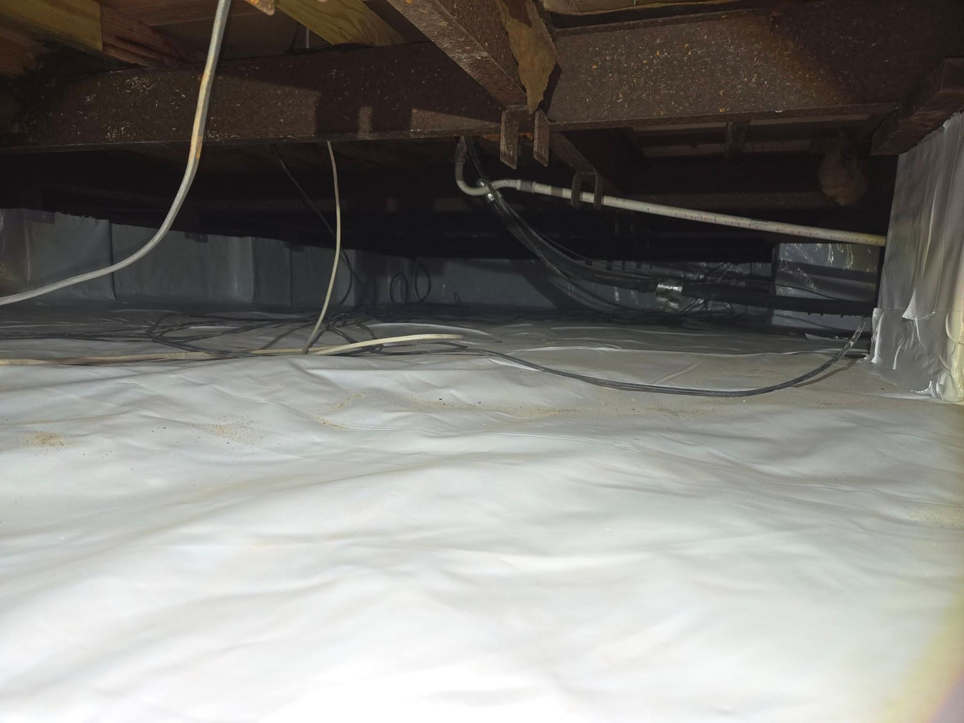 Plastic-covered crawl space with exposed floor joists and hanging wires