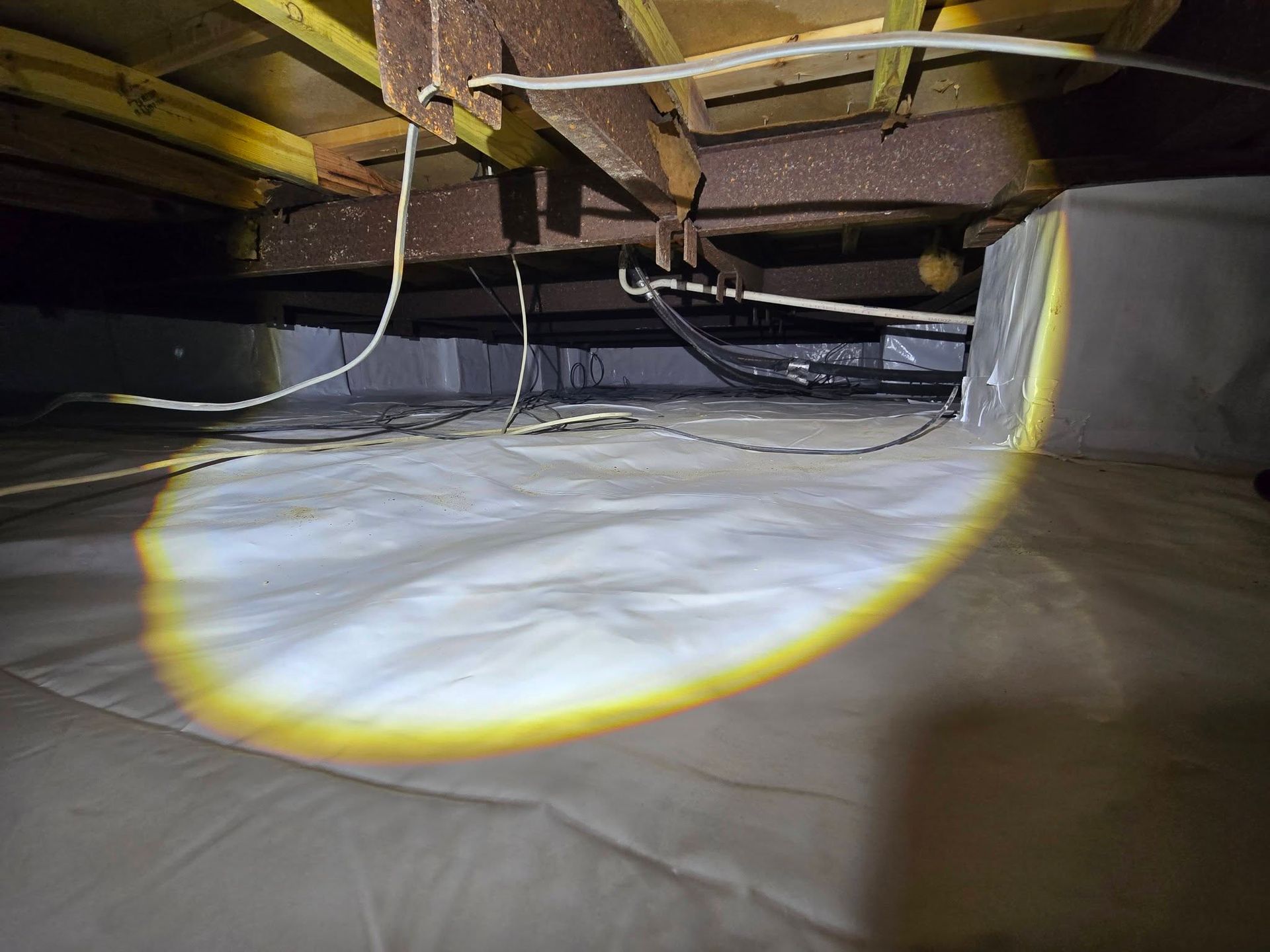 Flashlight beam under a house, illuminating the crawl space floor and exposed beams.