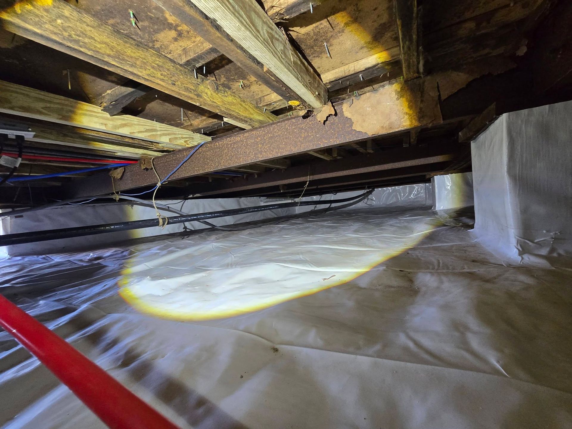 Flashlight illuminating plastic sheeting and wooden joists in a crawl space