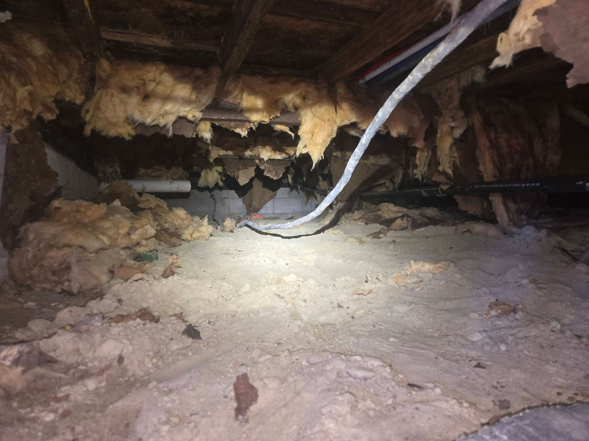 Dim cave interior with rocky walls and a pale hanging tube or pipe over a sandy floor