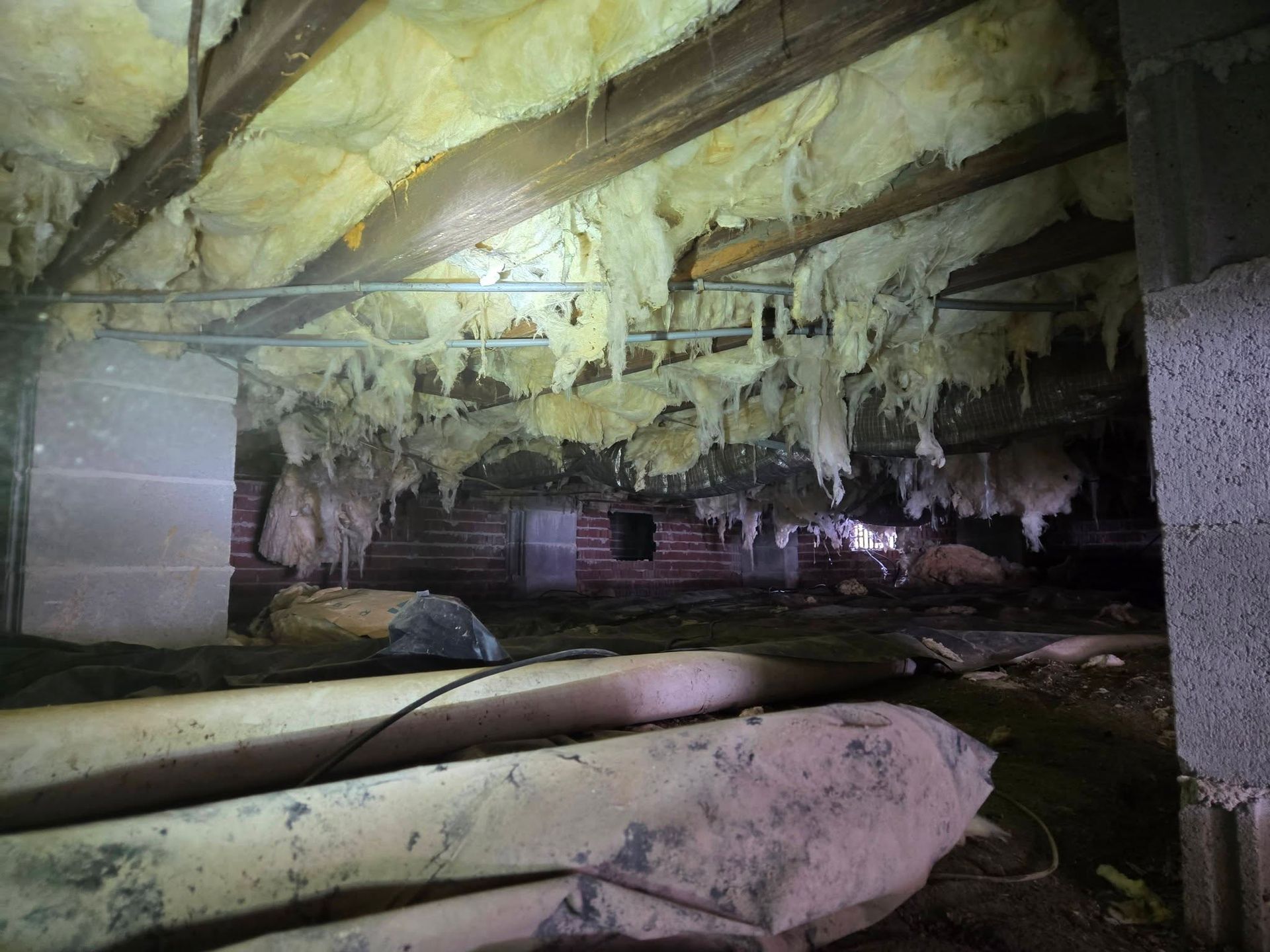 Damaged basement with hanging insulation, exposed beams, and debris-covered floors