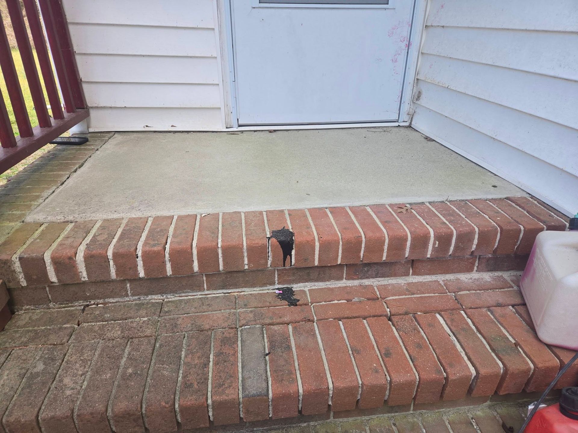 Brick front steps and porch with a small black object on the middle step near the front door
