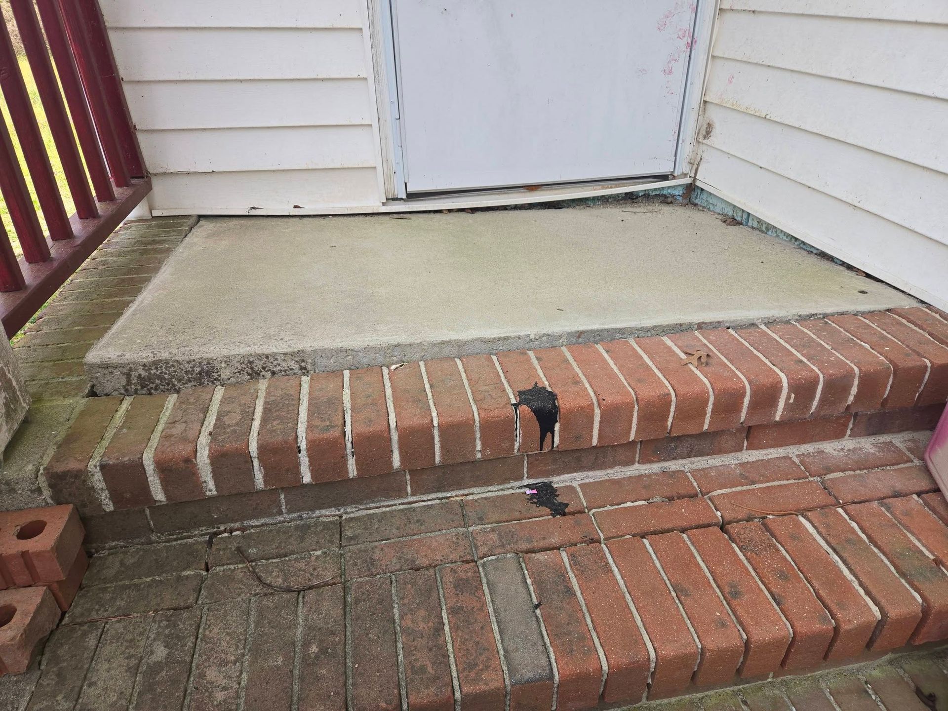 Brick front steps with a small black cat near the bottom and a white door at the top.