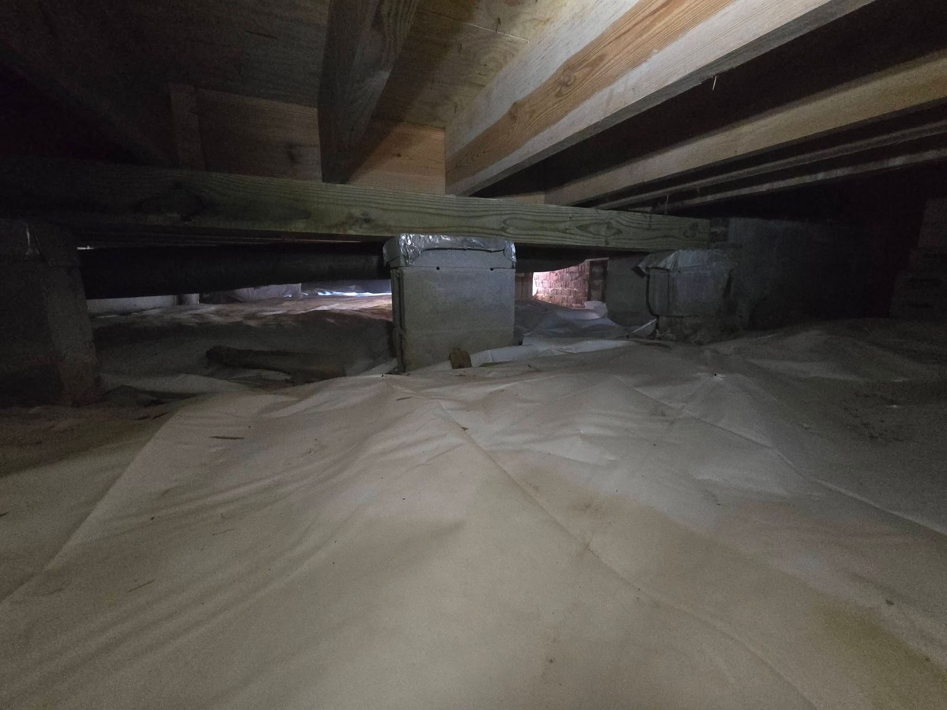 Crawl space under a house with a dirt floor, wooden beams, and a concrete support column.