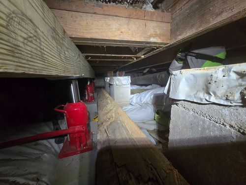 Crawlspace with red jack post supporting wooden beams and insulation along the floor and walls