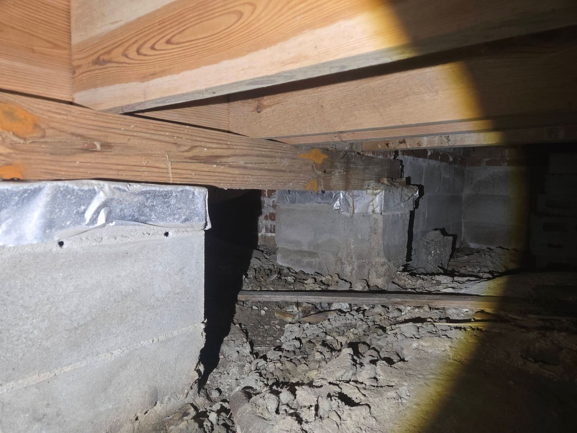 Damaged basement floor joist area with broken concrete and debris under a wooden beam