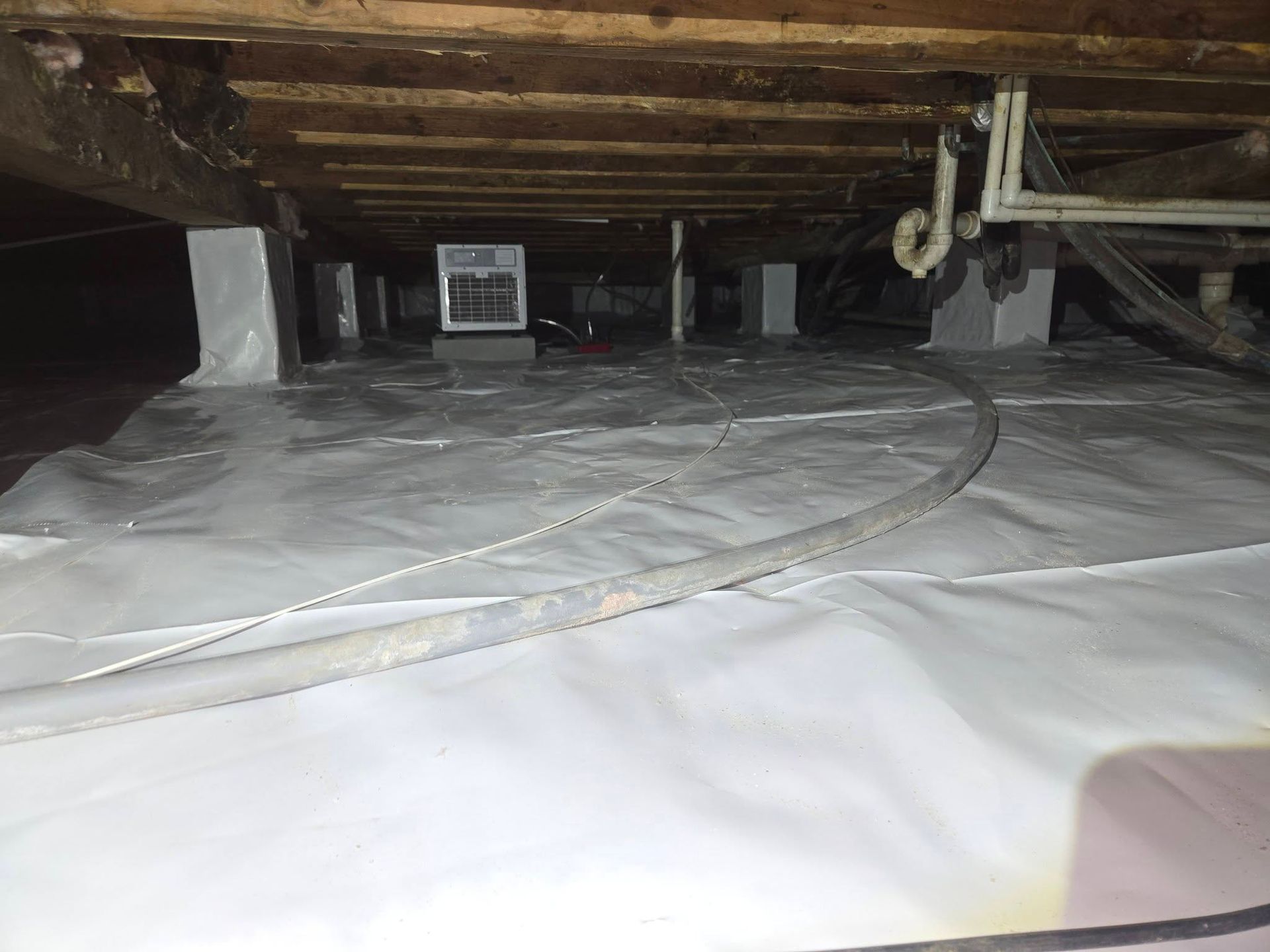 Crawlspace under wooden floor with white vapor barrier and exposed beams and vents
