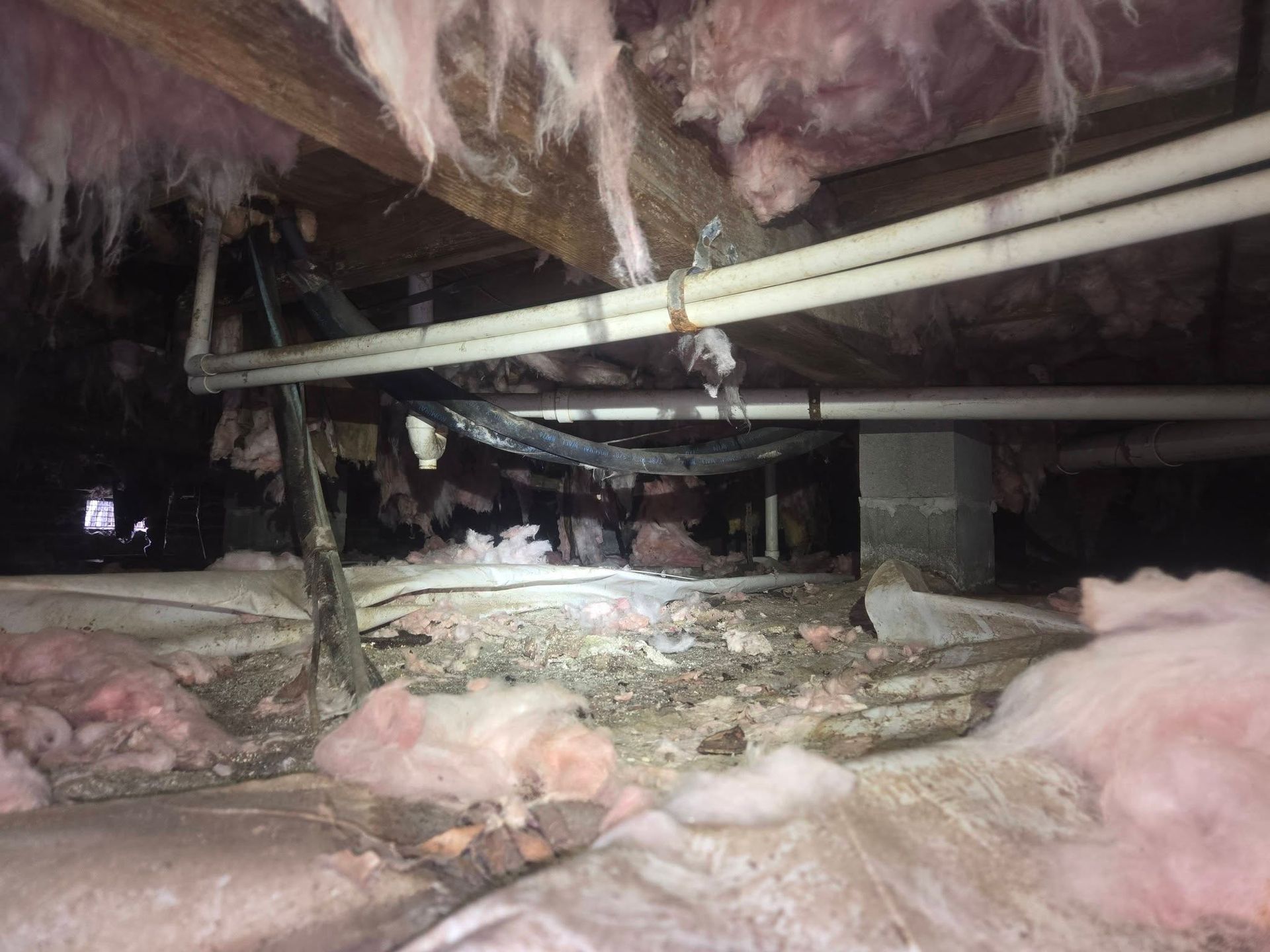 Damaged attic with torn pink insulation, exposed beams, and debris scattered on the floor