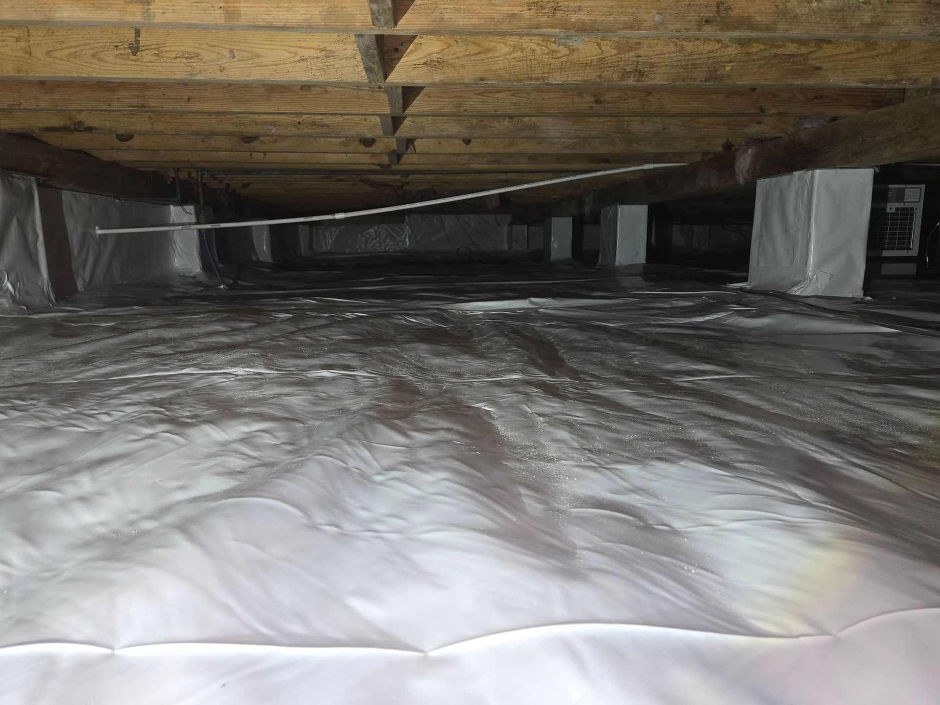 Crawl space with exposed wooden beams and a white plastic vapor barrier covering the floor.