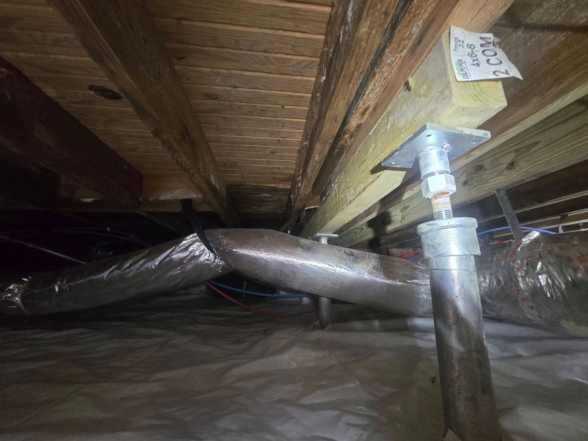 Insulated ductwork and a metal pipe under floor joists in a crawlspace of a house