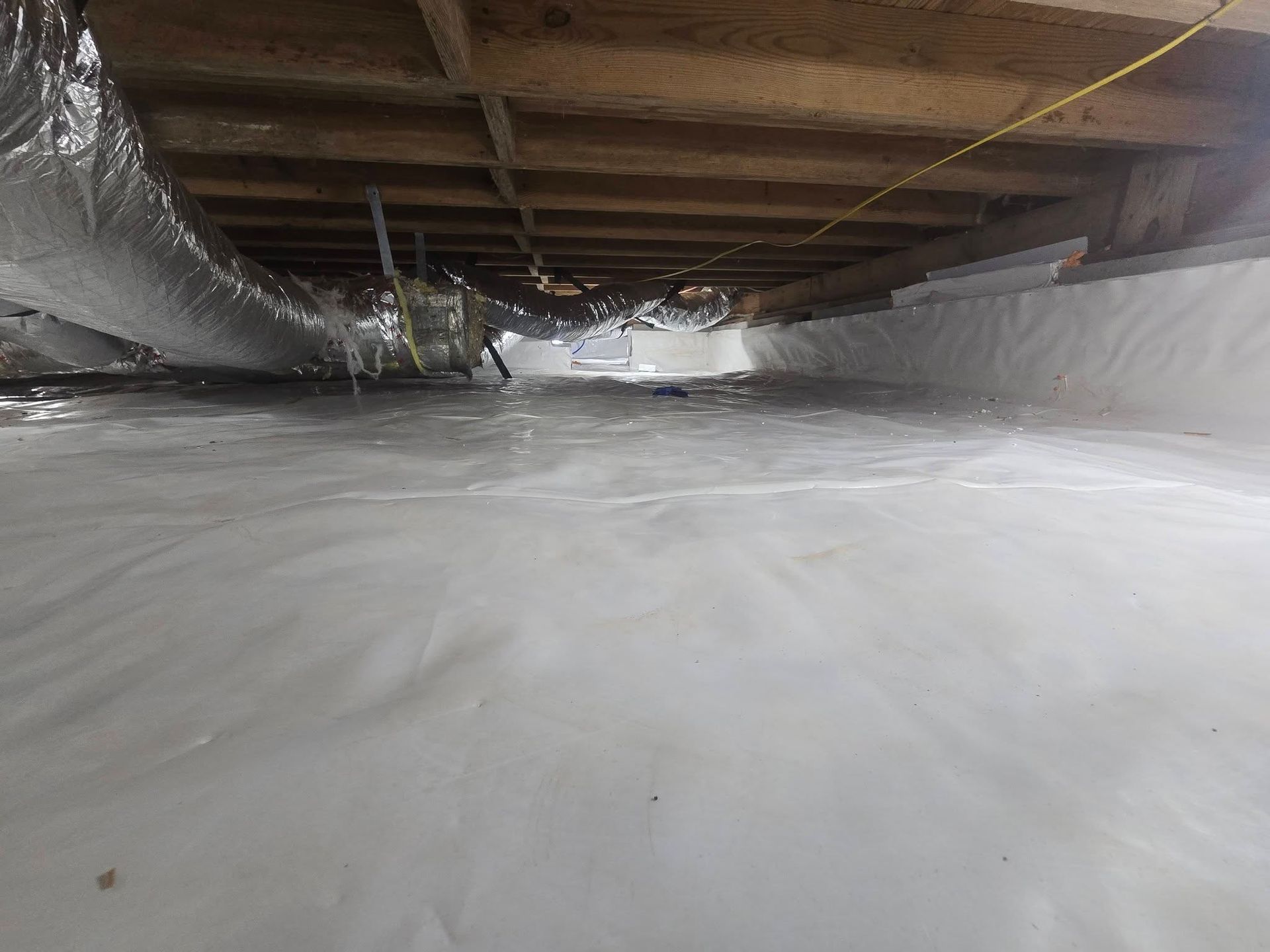 Plastic-covered crawlspace with exposed wooden beams and insulation under the floor
