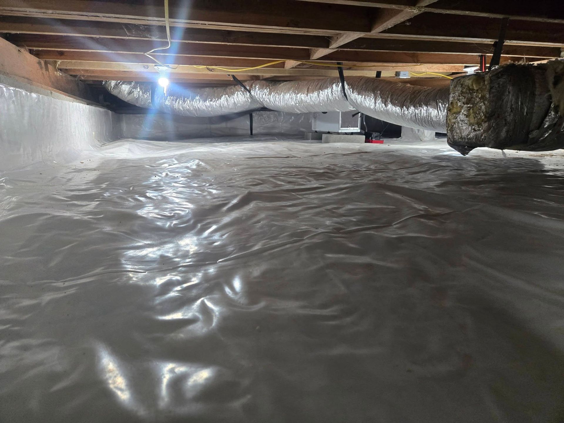 Floodwater flowing under a low wooden crawlspace with beams and insulation visible above.