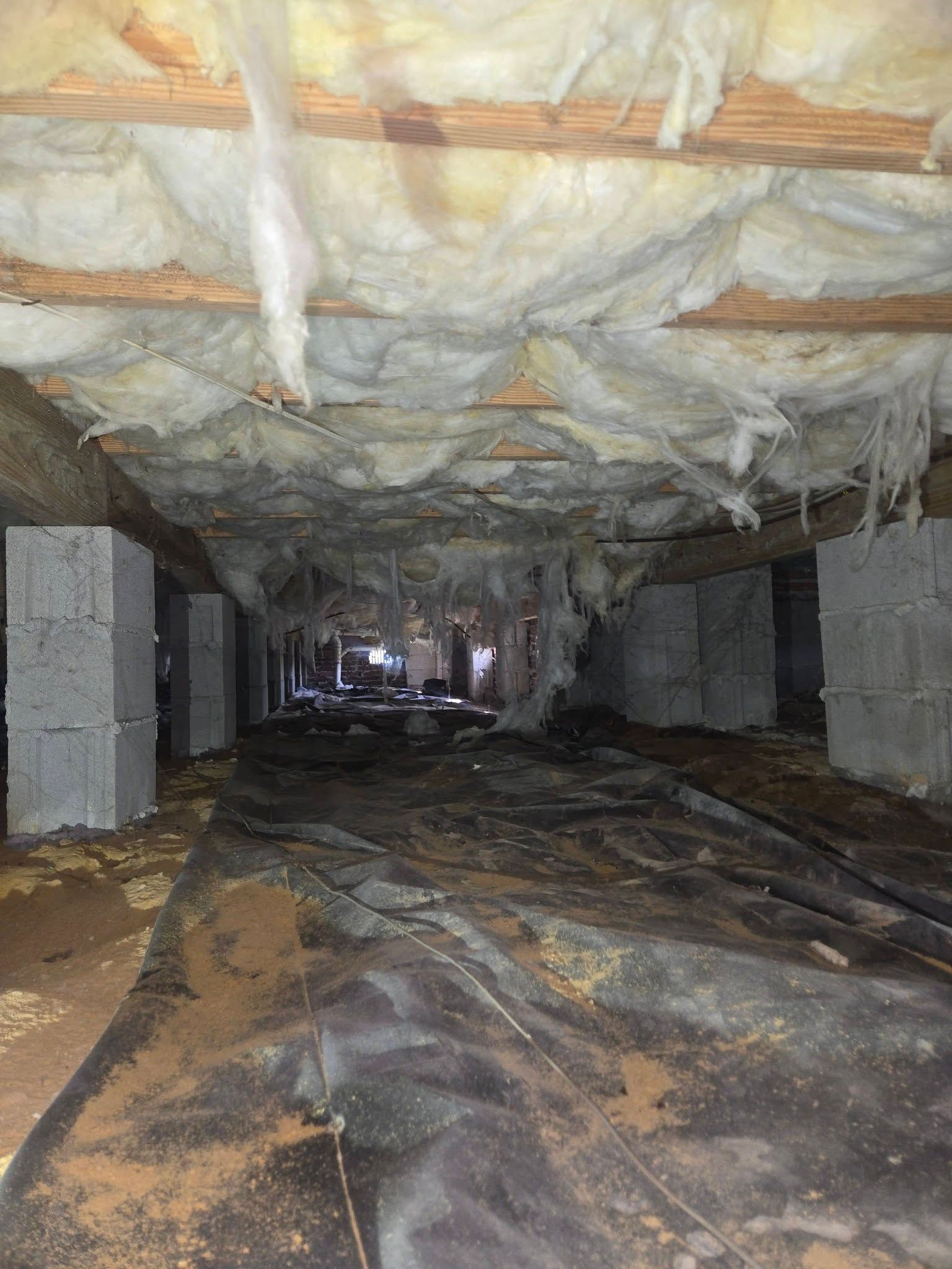 Flood-damaged crawlspace with wet insulation hanging from the ceiling and debris-covered floor