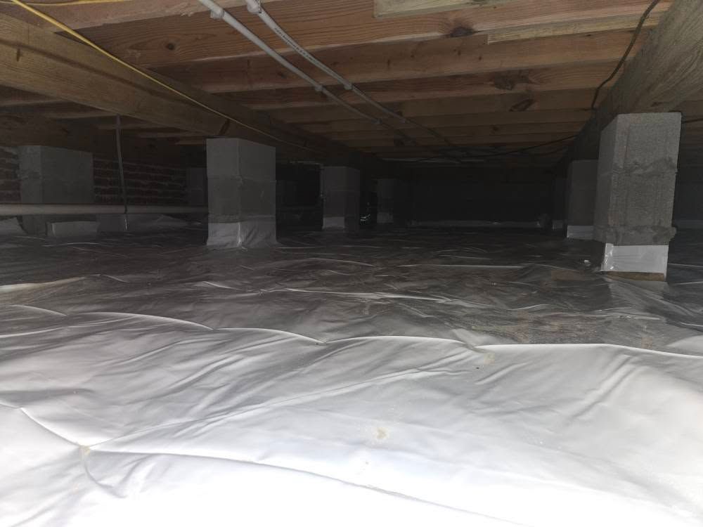 Crawlspace with plastic sheeting on the floor, concrete support pillars, and exposed wooden beams overhead.