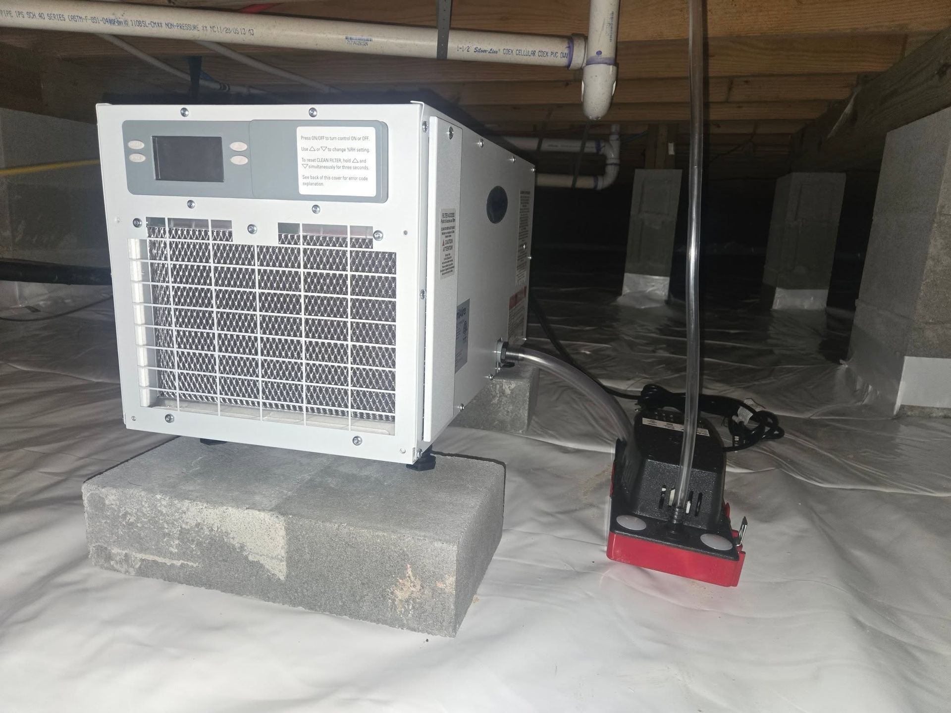 Portable generator on cinder blocks under a house, with a red-and-black jack nearby on white sheeting.