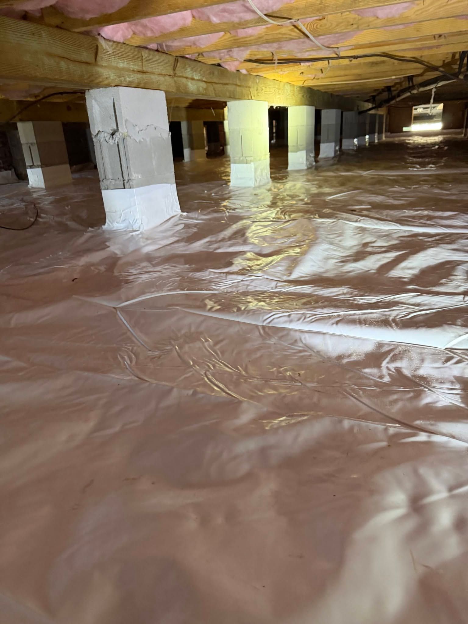 Crawlspace flooded with standing brown water beneath support beams and insulation.