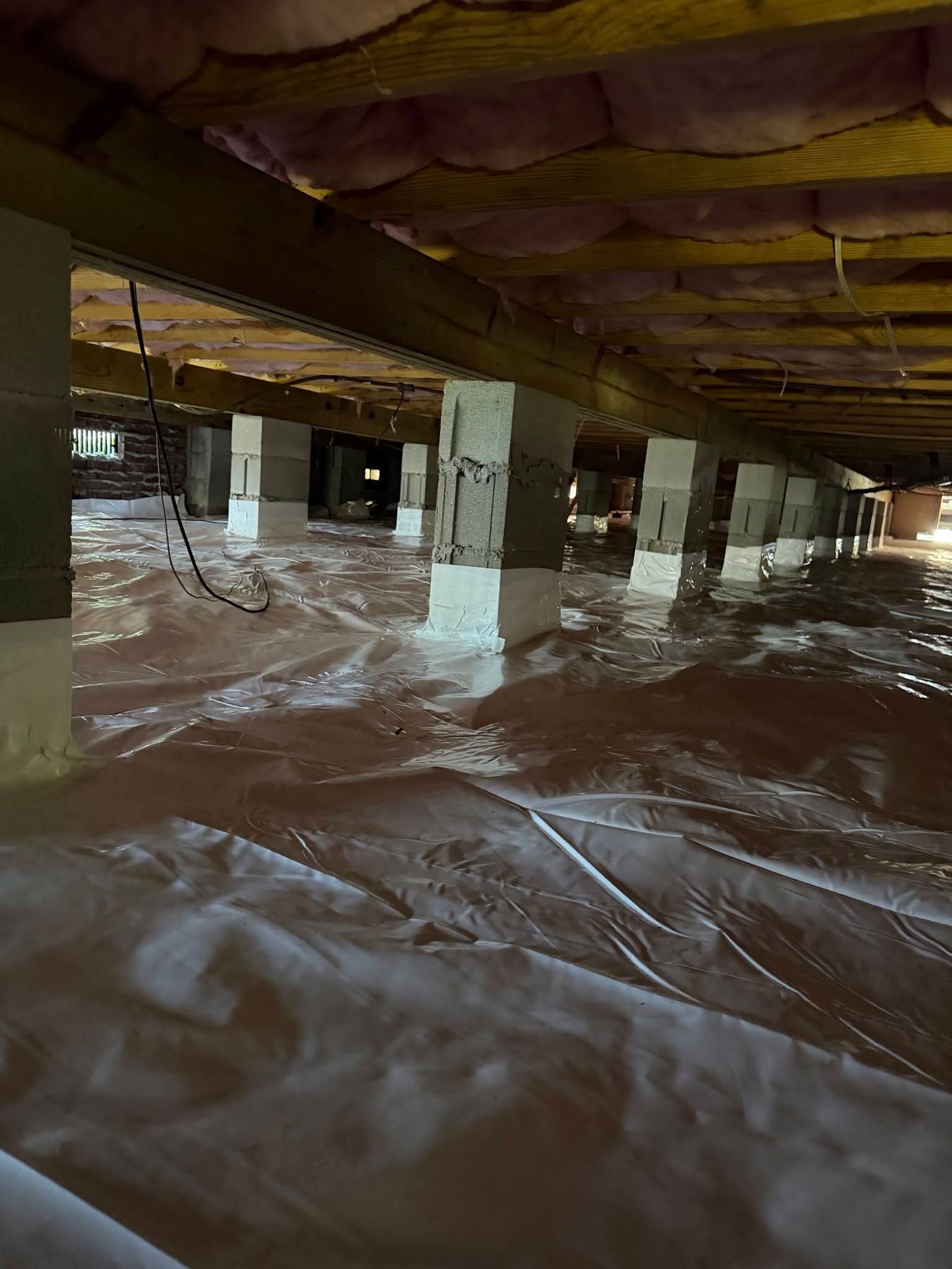 Basement crawlspace with exposed beams, support posts, and plastic sheeting covering the floor