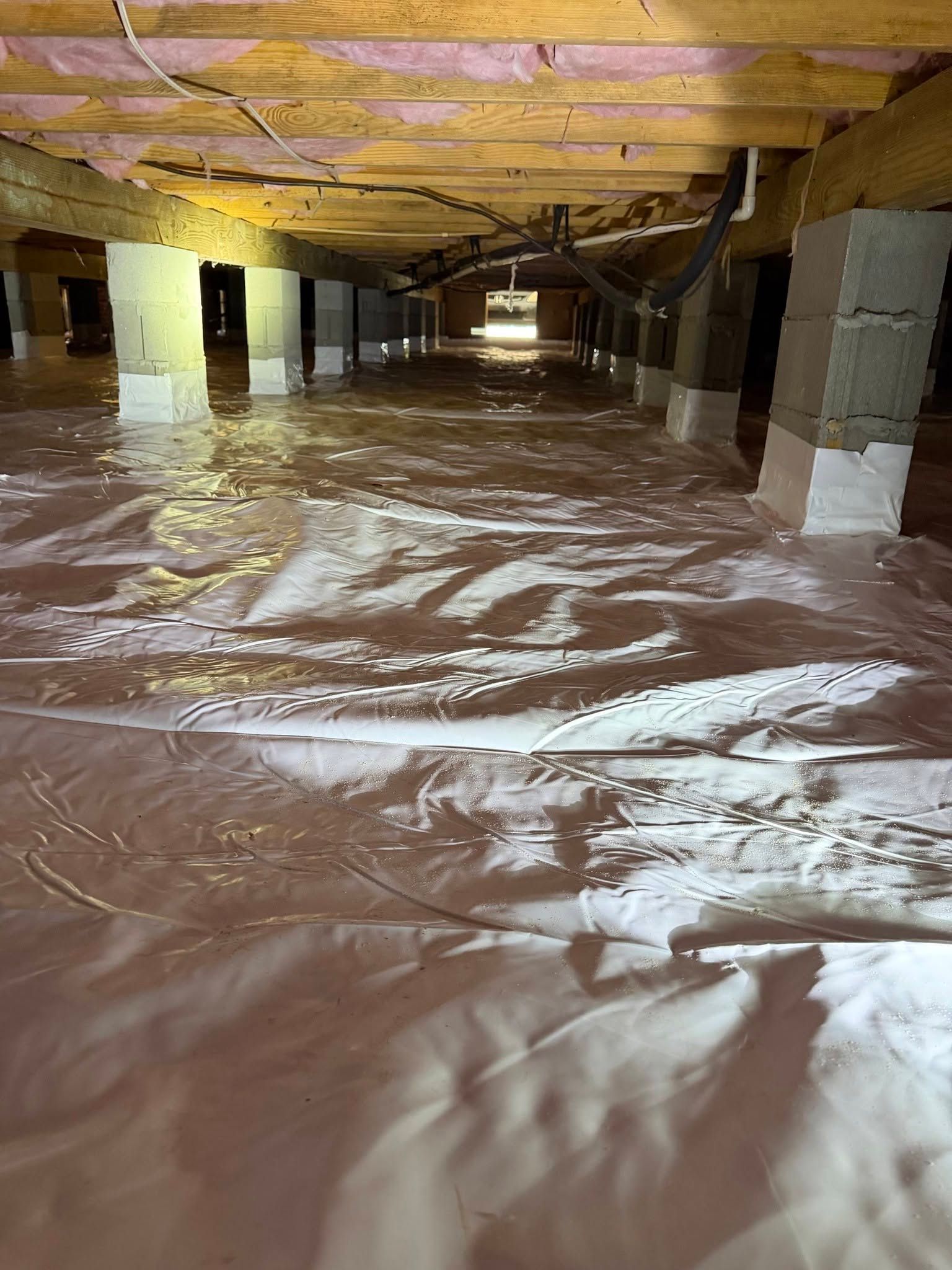 Large crawl space with plastic sheeting covering the floor and exposed wooden beams overhead