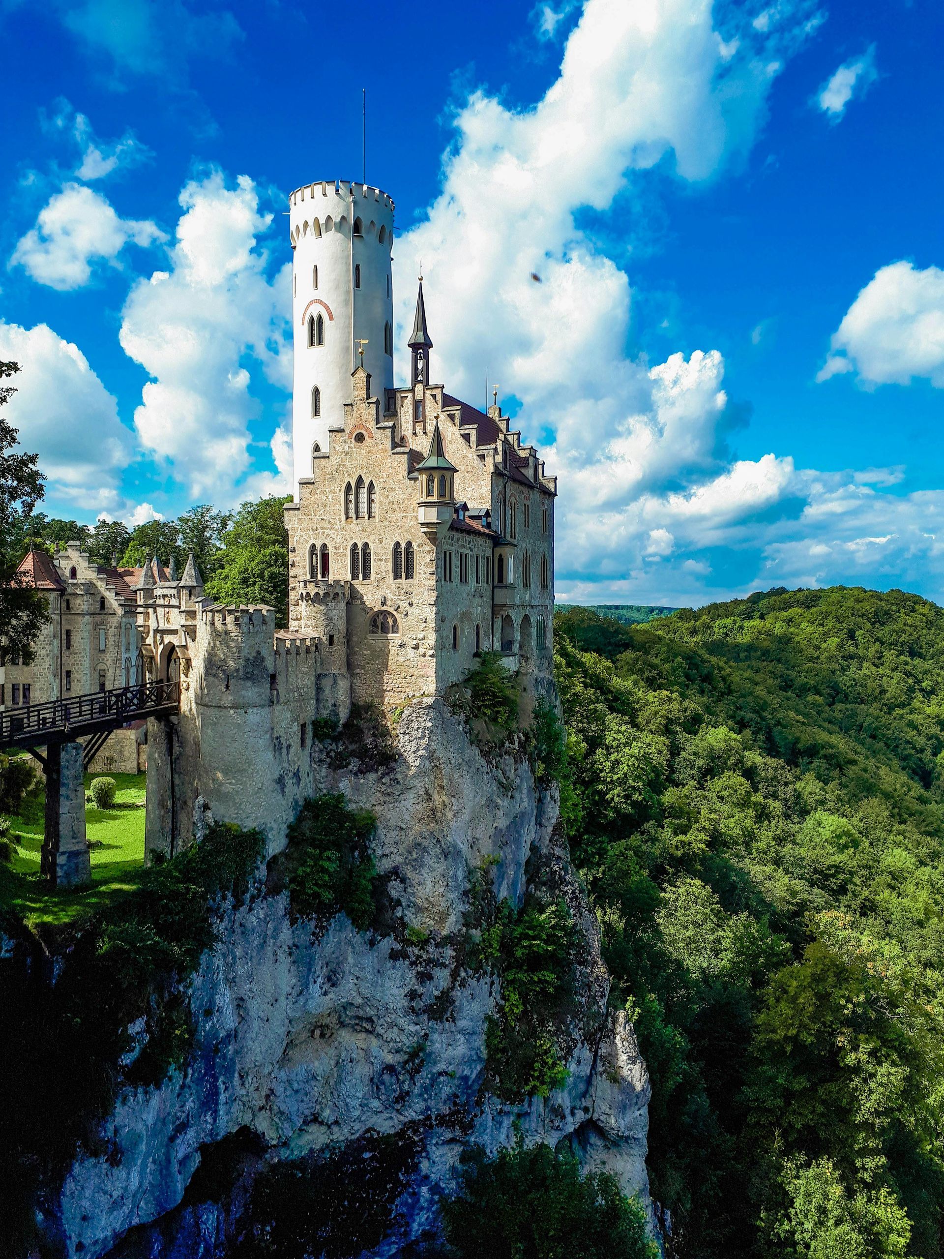 Schloss Liechtenstein thront auf einem Felsen, ein hoher weißer Turm vor strahlend blauem Himmel.