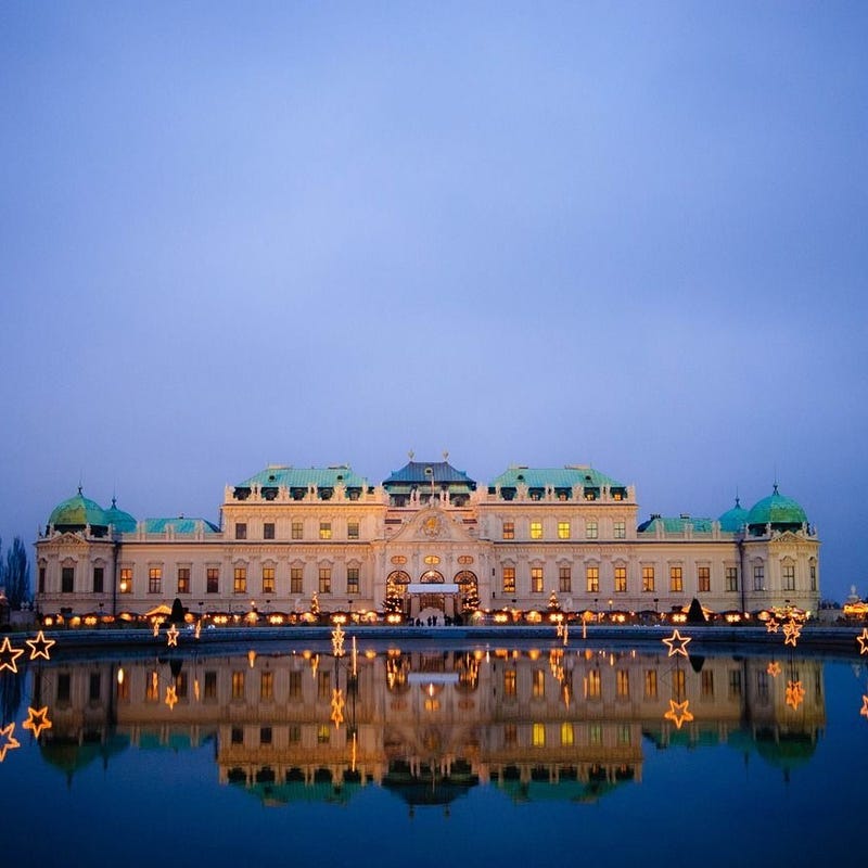 Der Belvedere-Palast, der sich in der Abenddämmerung im Wasser spiegelt und von warmem Licht erhellt wird.