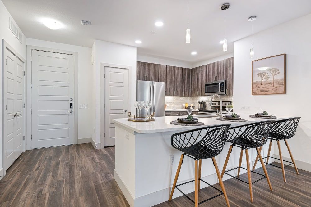 Modern white kitchen with wood cabinets, island seating, stainless fridge, and dark bar stools