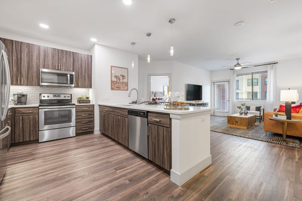 Open-concept kitchen and living room with stainless appliances, wood floors, and bright white walls