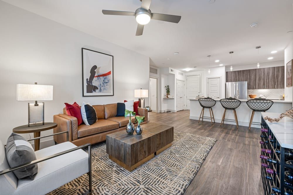 Modern living room with brown sofa, patterned rug, coffee table, and open kitchen with bar stools