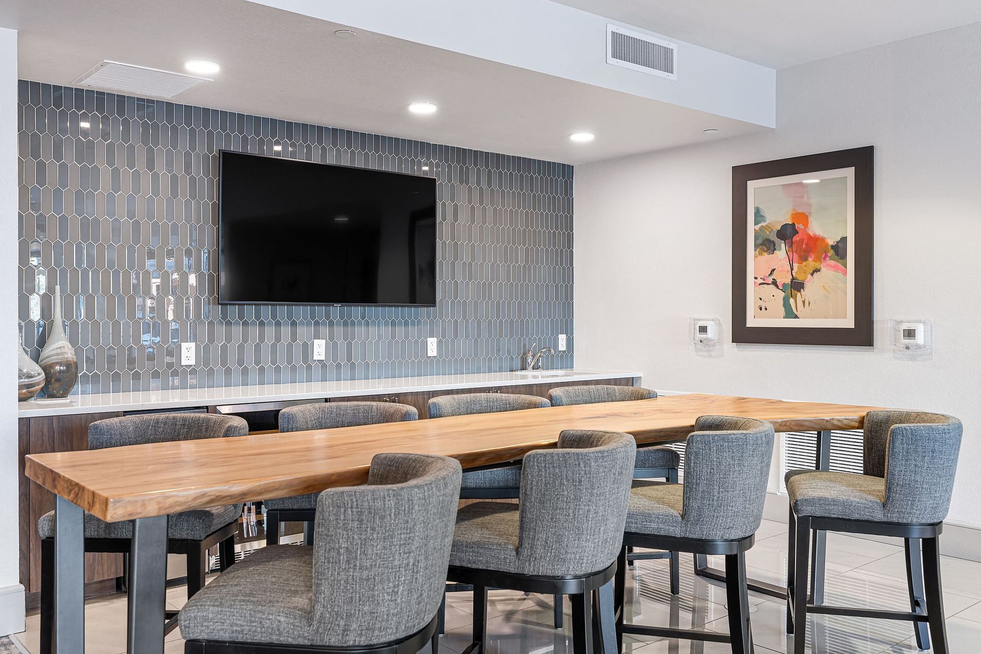 Modern lounge with wall-mounted TV, stone bar, wood counter, and gray upholstered stools