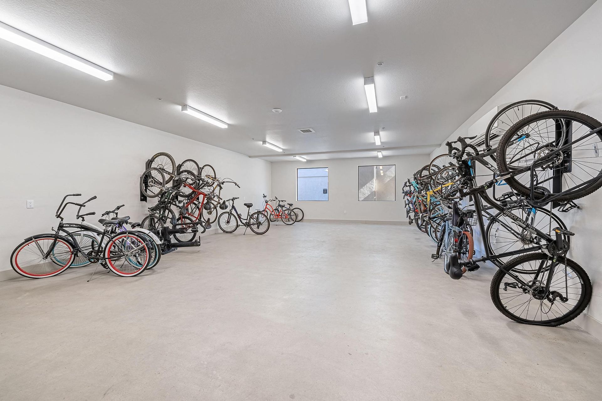 Bright bike storage room with many bicycles lined along both walls under fluorescent lights.