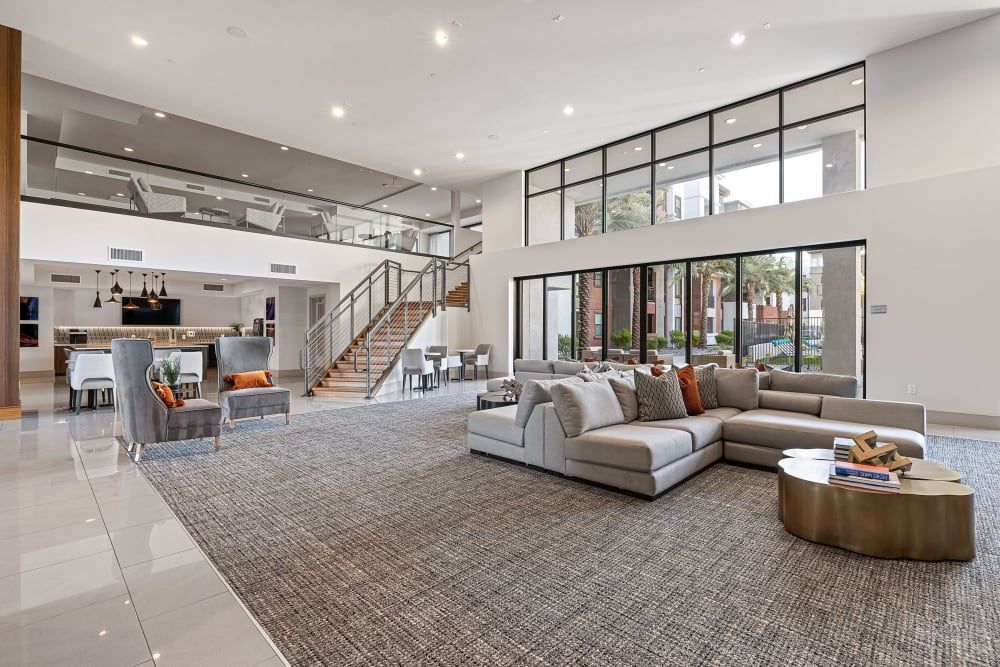Modern lobby with gray sectional, large windows, staircase, and kitchen area