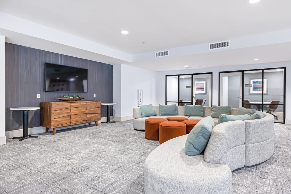 Modern lounge with curved white sectional, orange ottomans, TV, and gray accent wall
