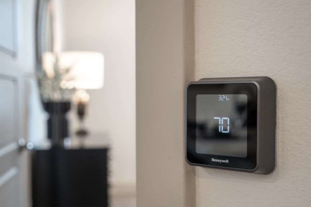 Honeywell thermostat on a wall in a softly lit home interior, showing 70°F.