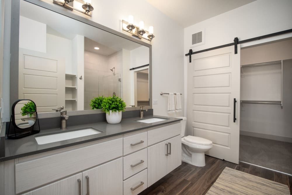Modern bathroom with double vanity, large mirror, sliding barn door, and walk-in closet view