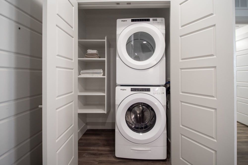 Stacked washer and dryer in a small white laundry closet with shelves and open doors