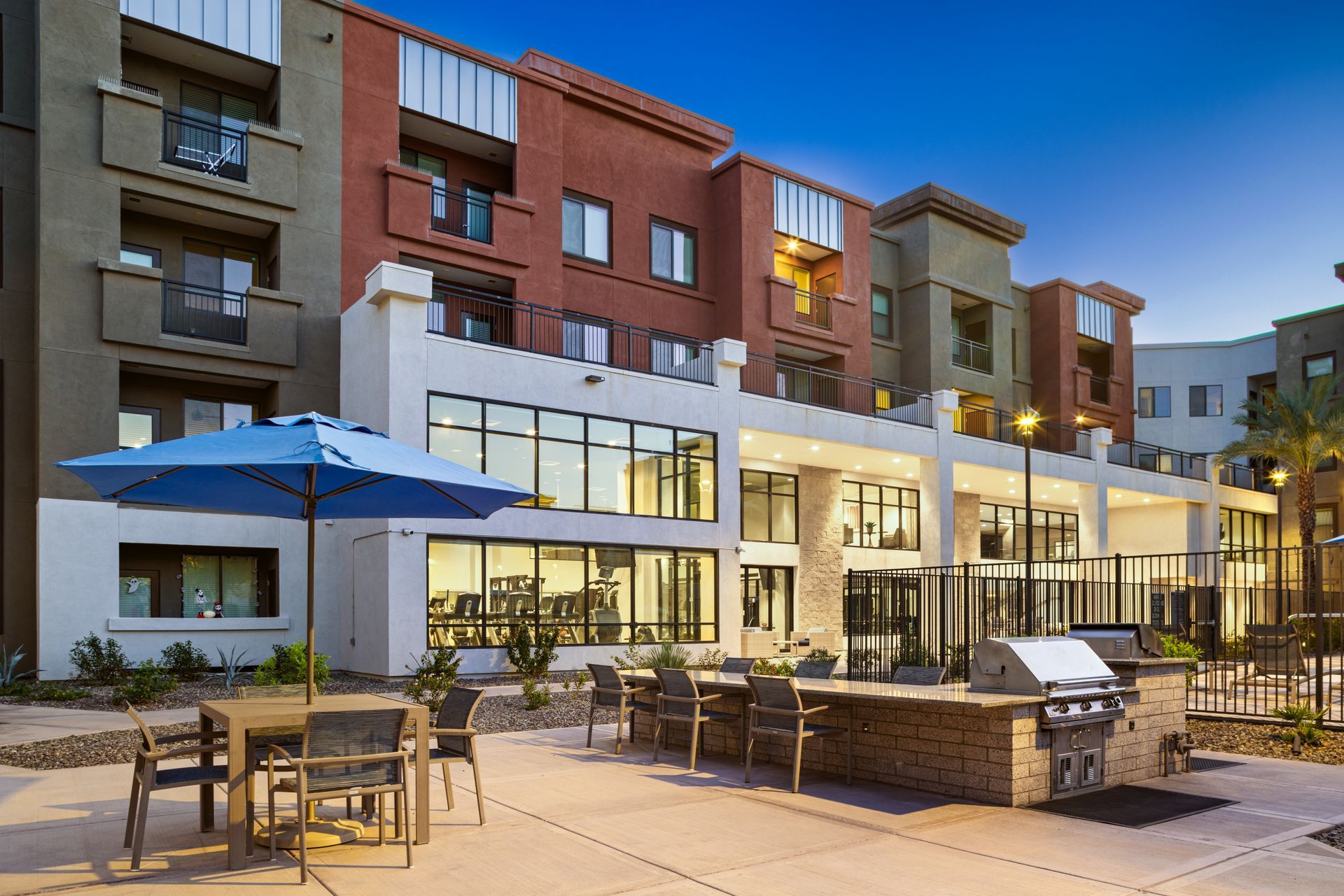 Outdoor courtyard with patio seating and a grill in front of modern apartment buildings at dusk