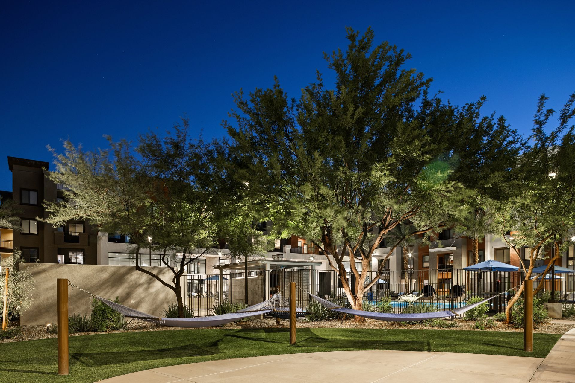 Courtyard with trees, lawn, and a small pool outside apartment buildings at dusk