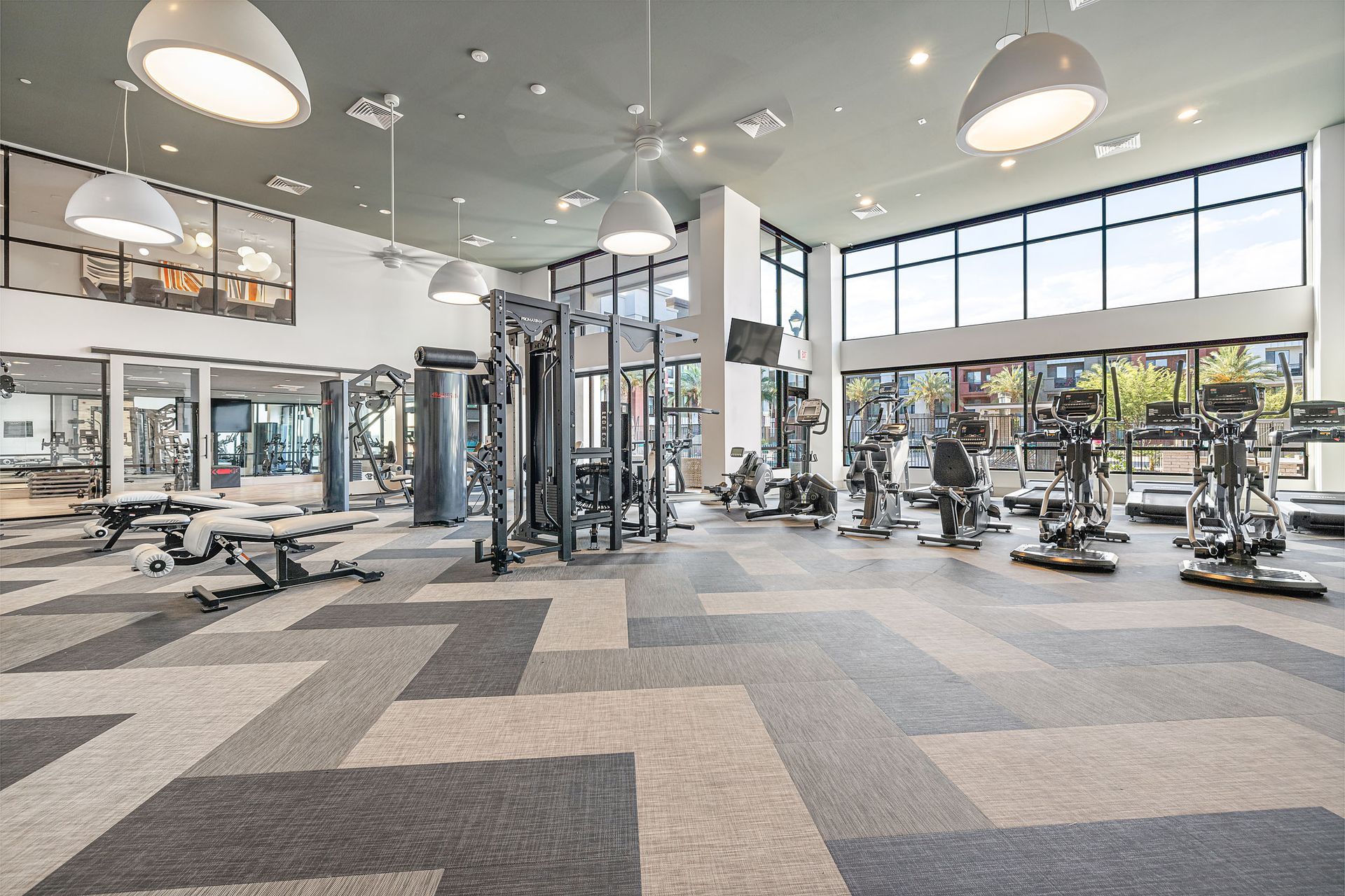 Modern gym interior with exercise machines, large windows, and gray carpeted flooring