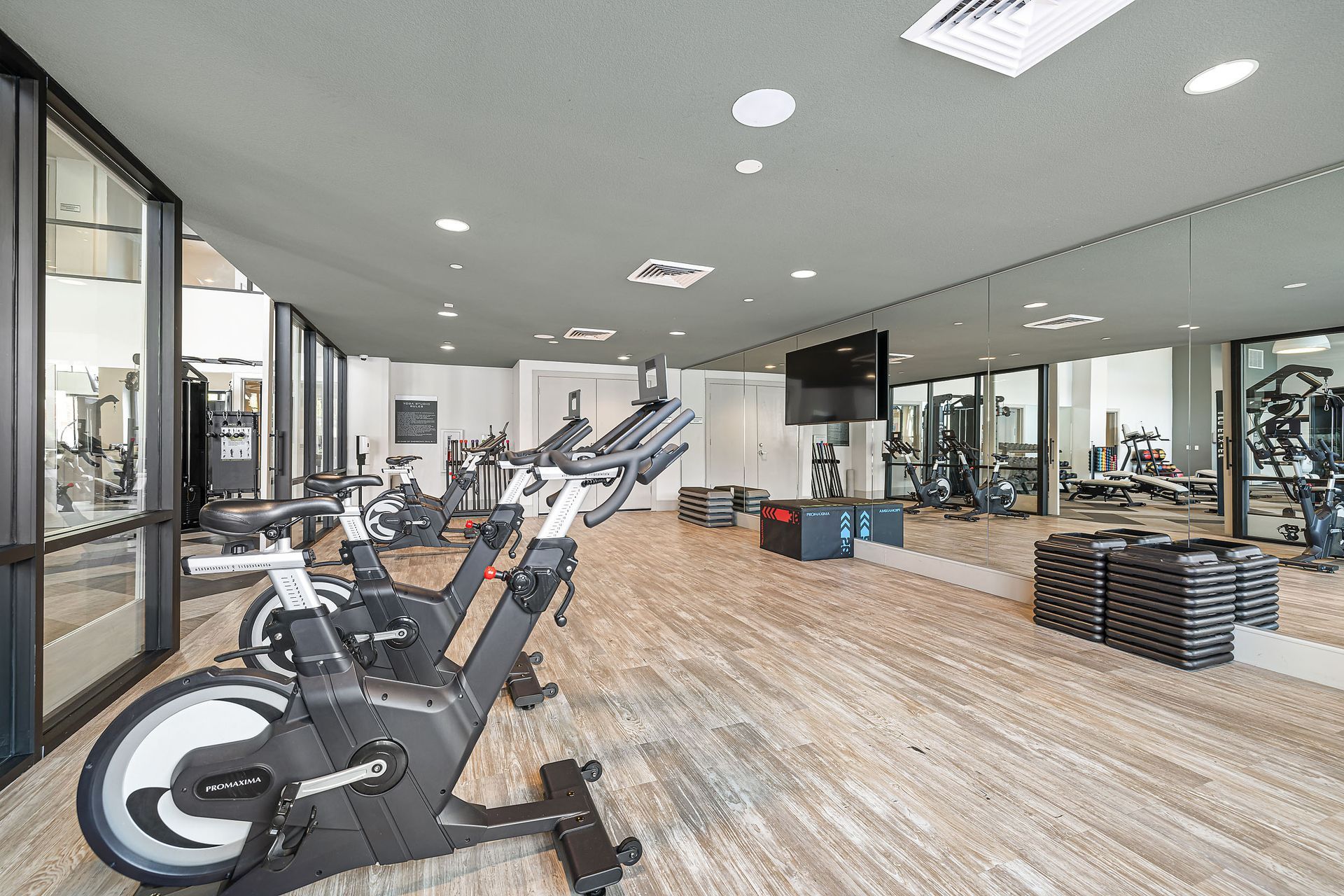 Modern gym with exercise bikes, treadmills, mirrors, and wood flooring