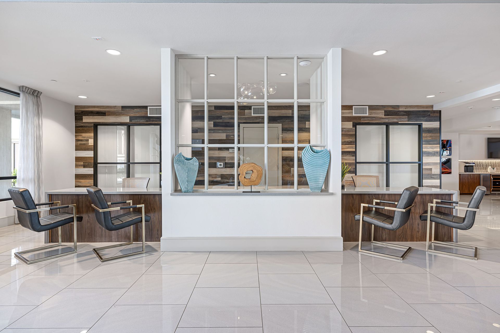 Modern lobby with white tiles, glass partitions, and blue vases between matching lounge chairs.