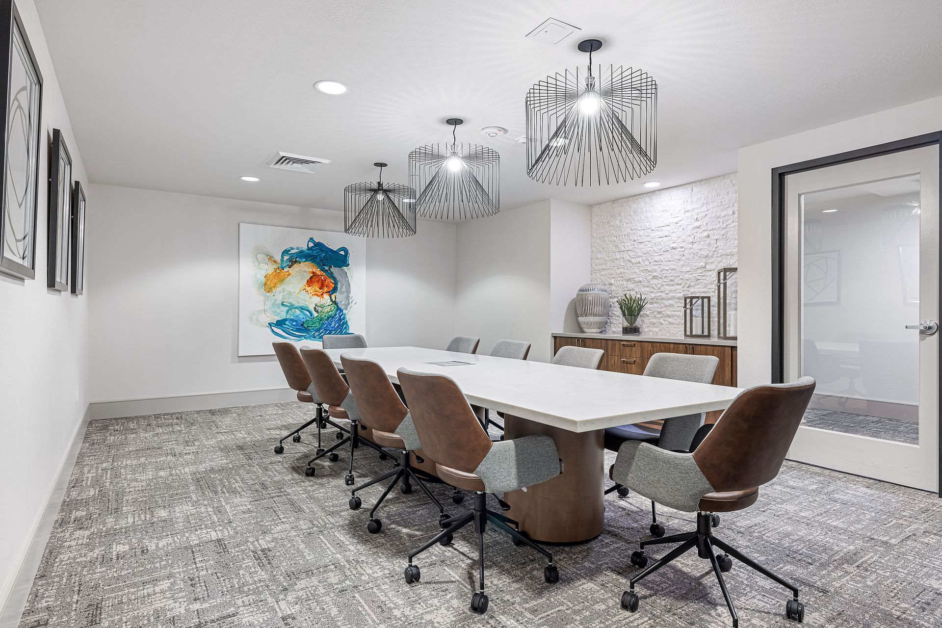 Modern conference room with a long white table, brown chairs, and decorative wall art on a gray patterned carpet.