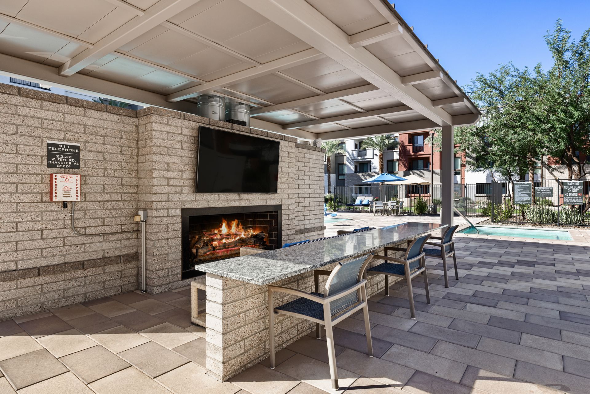 Outdoor covered patio with stone fireplace, dining tables, and lounge chairs by a pool