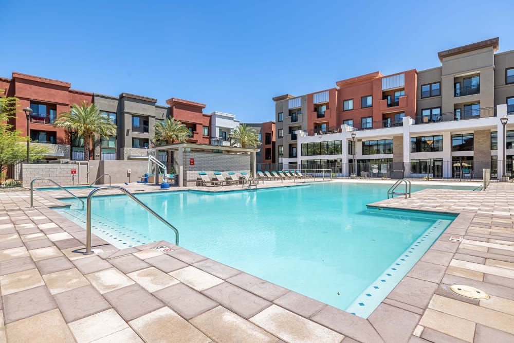 Apartment courtyard with a large swimming pool, lounge chairs, and modern brick buildings around it