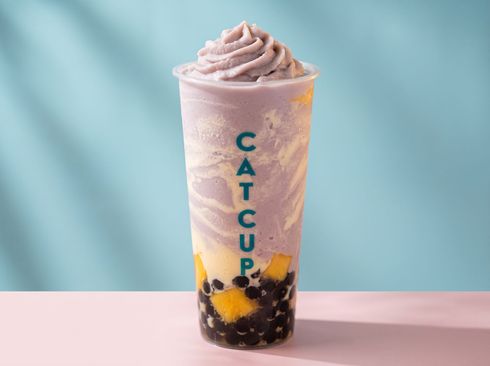 Tall pastel lavender bubble tea with black tapioca pearls and a whipped top on a pink surface