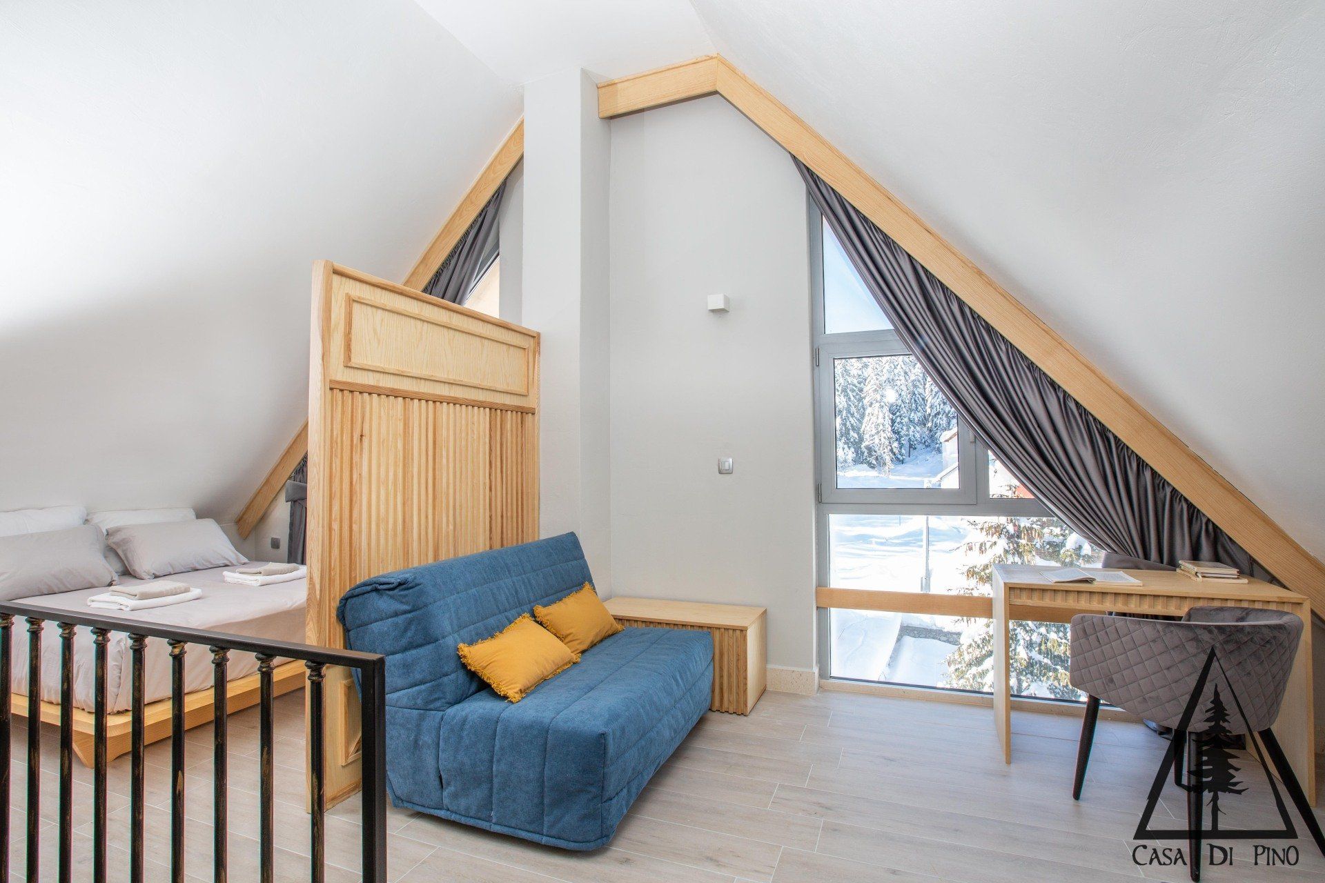 A bedroom in a penthouse hotel apartment with a blue couch and a desk and big windows.