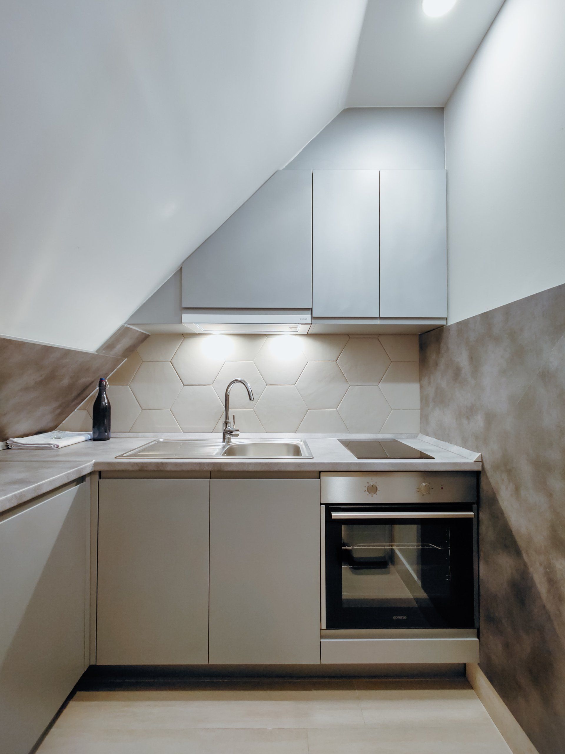 A kitchen with a sink stove and oven under a slanted ceiling