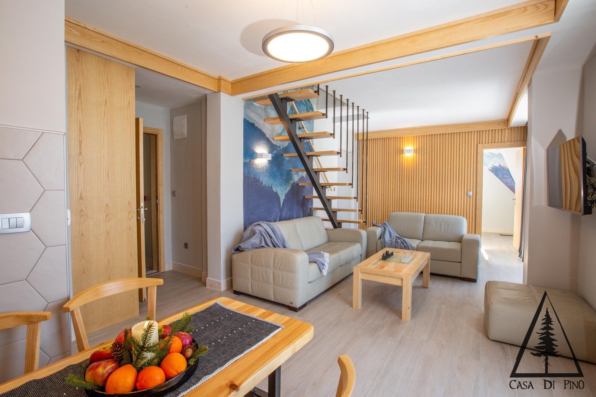 A living room in a hotel penthouse with a couch, table, chairs and stairs.