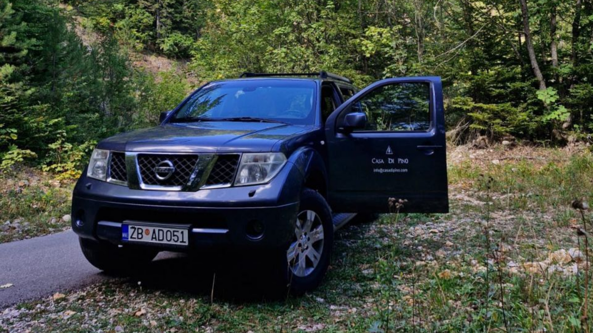 Dark blue Nissan Pathfinder SUV with an open door parked on a forest road.