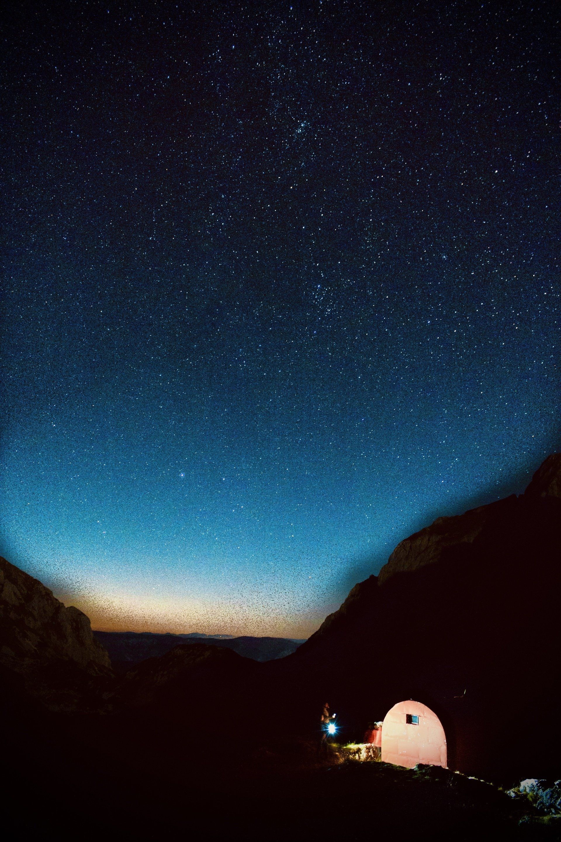A tent is lit up under a starry night sky