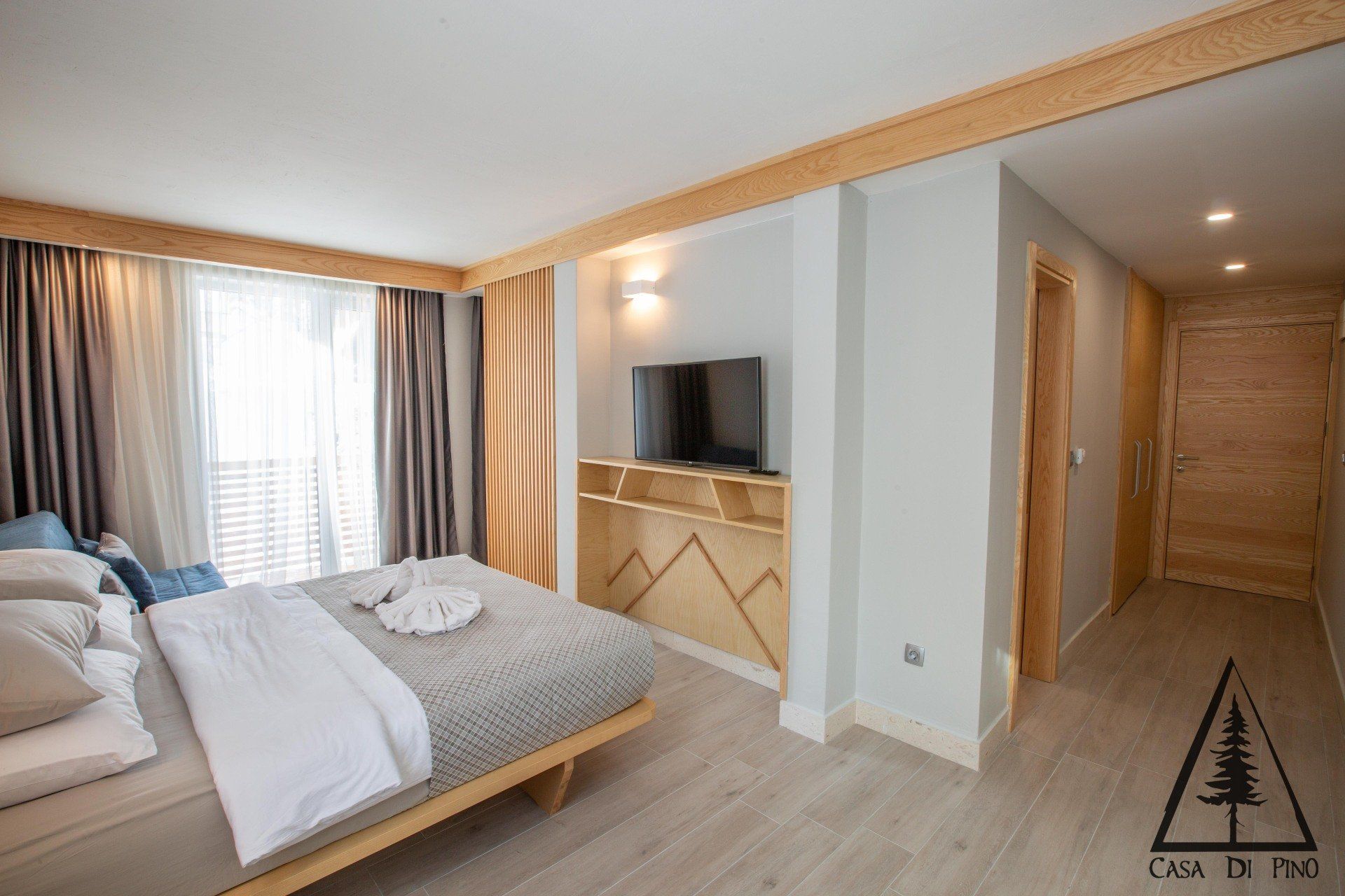 A bedroom with a large bed and a flat screen tv with wodden details on the wall.